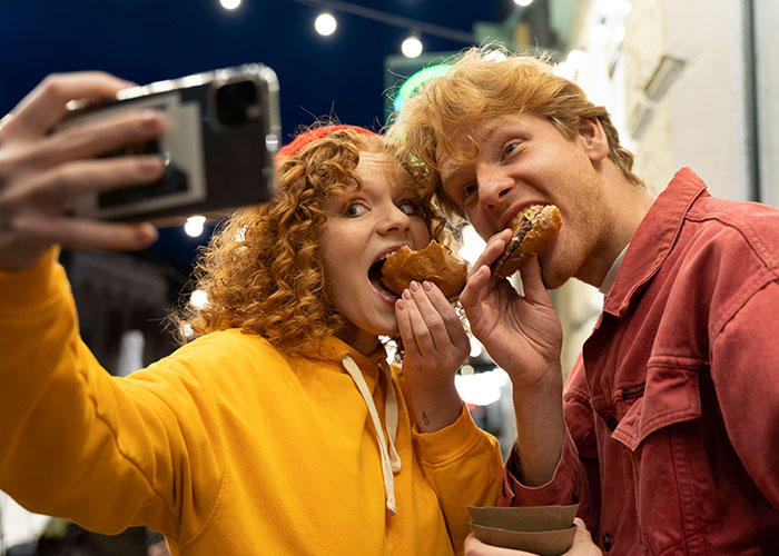 Couple taking a selfie while eating donuts, capturing a candid moment that might change how they see each other.