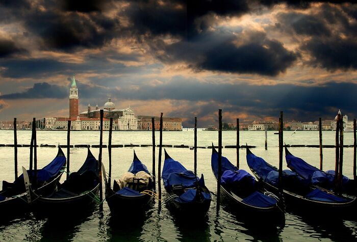 Venice gondolas under dramatic skies, capturing a disappointing tourist experience influenced by FOMO.