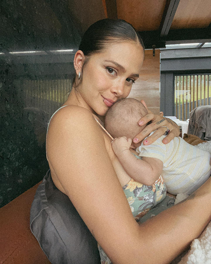 Singer Greeicy holding her baby close, showcasing a serene motherhood moment indoors.