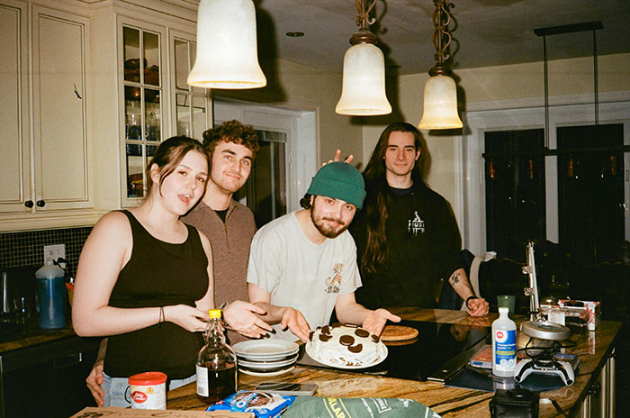Friends in a kitchen, one wearing a beanie, preparing a meal together, laughing and enjoying their time.