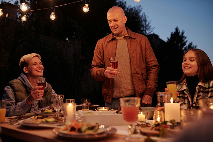 Man with friends at outdoor dinner, holding a drink.