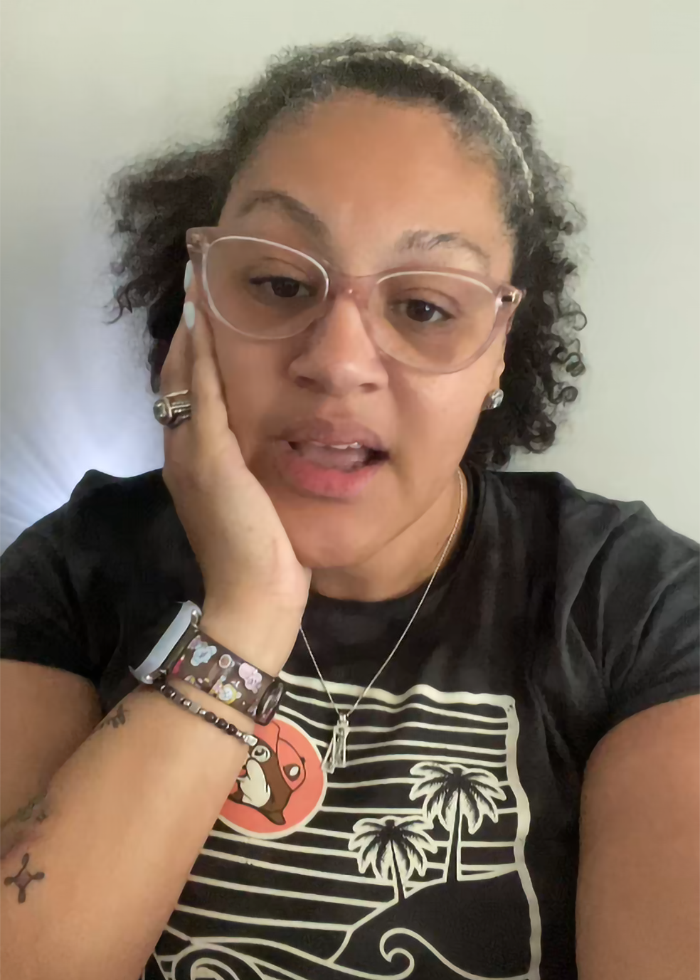 Woman wearing glasses and a black shirt speaking about inappropriate wedding guest dress causing mass debate.