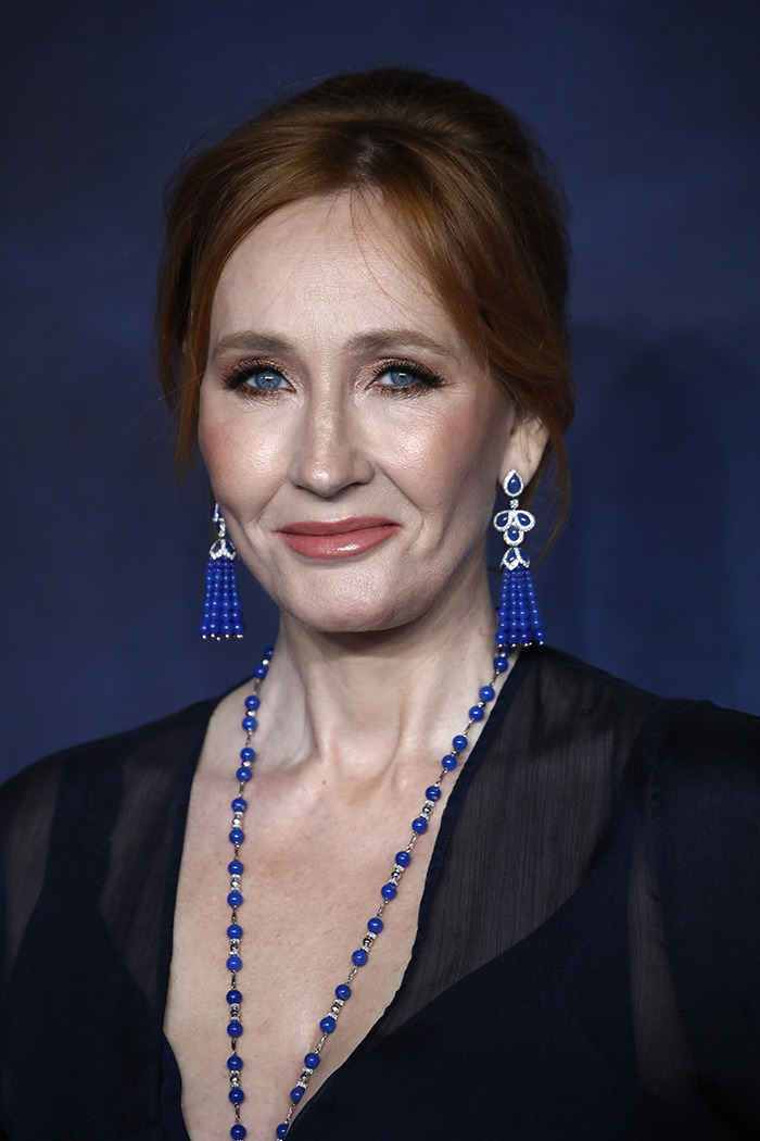 JK Rowling smiling at an event, wearing blue necklace and earrings, following trans ruling celebration.