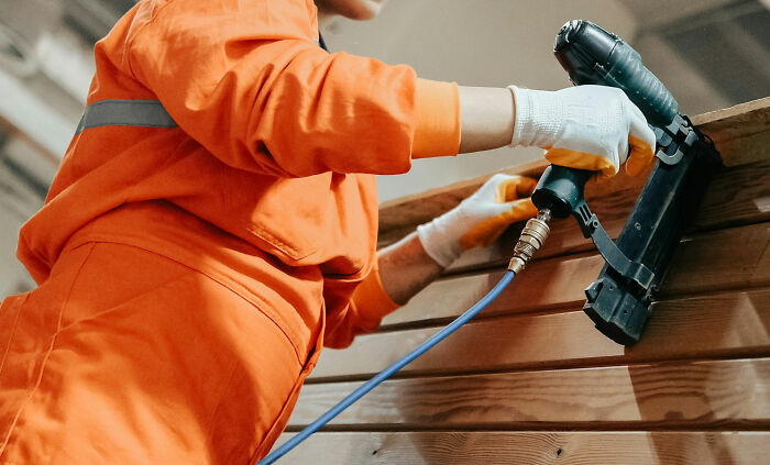Person in orange uniform using a power tool on wooden planks.