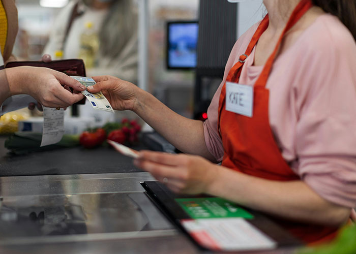 Grocery store employee in uniform assisting a customer at checkout, adhering to store policy. Grocery store employee in uniform assisting a customer at checkout, adhering to store policy.