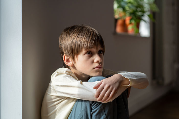 Child in light room, sitting with knees up, related to housemate mom topic.