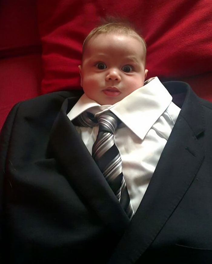 A baby humorously dressed in an oversized suit and tie, showcasing funny men.
