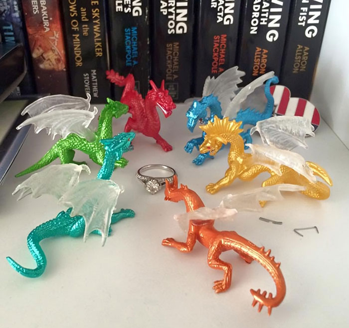 Toy dragons arranged around an engagement ring, making life amusing for their partners.