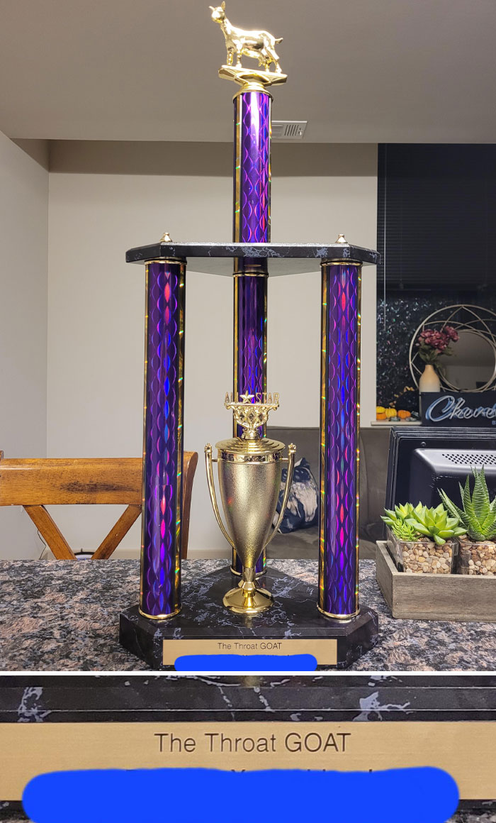 Golden "Throat GOAT" trophy with purple columns, showcasing hilarious men's antics at home.