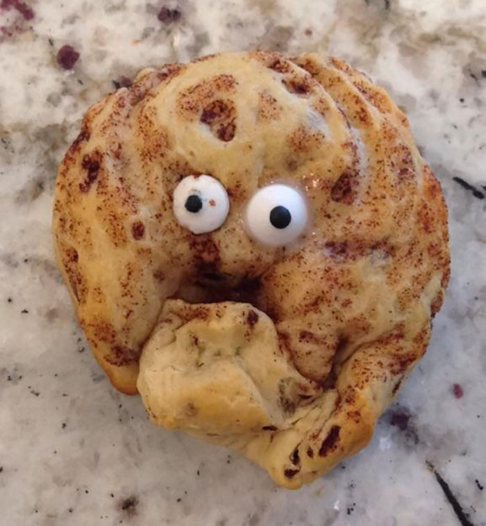 Cinnamon roll with googly eyes on a marble counter, resembling a distressed face, embodying "worse day than you" humor.