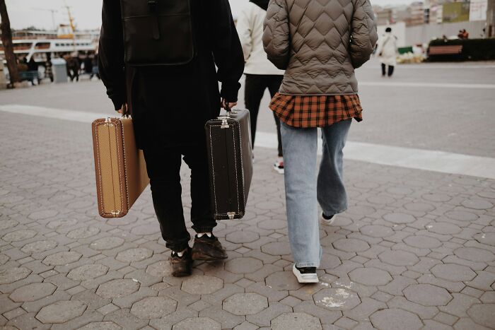 Two people carrying luggage, walking outside, hinting at a family vacation scenario.
