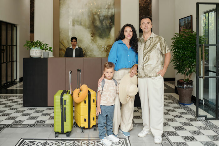 Family ready for vacation with luggage in hotel lobby, mom excited and nervous.