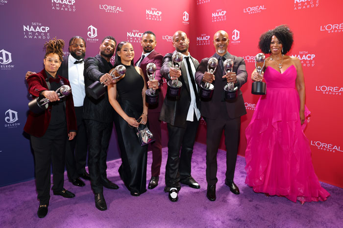 Group of film legends holding awards at the NAACP Image Awards, posing on a purple carpet.