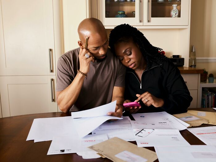 Couple reviewing documents and using a smartphone, focusing on homeowner first home tips in a kitchen setting.