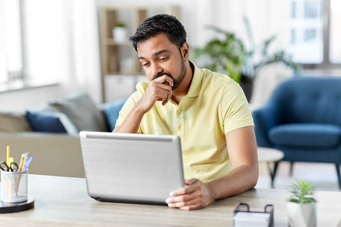 Man in yellow shirt, sitting at a desk in a cozy living room, using a laptop while considering first-home tips for homeowners.