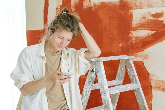 Person checking phone next to a ladder and freshly painted wall, illustrating homeowner first home tips.