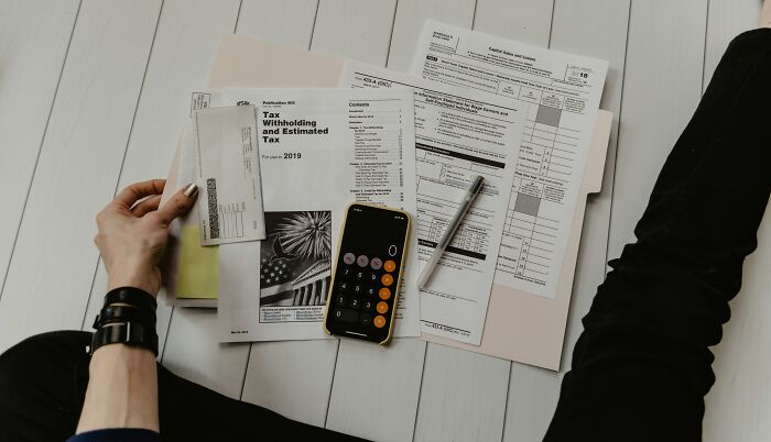 Person reviewing tax documents and financial papers on floor, using a calculator; homeowner first home tips concept.