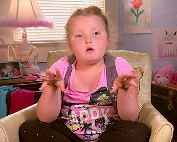 Young girl in a colorful outfit sitting in a decorated room, gesturing with hands, from Toddlers & Tiaras.