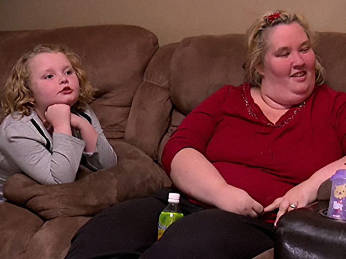 Young girl sitting on a couch next to a woman in red, both appearing relaxed.