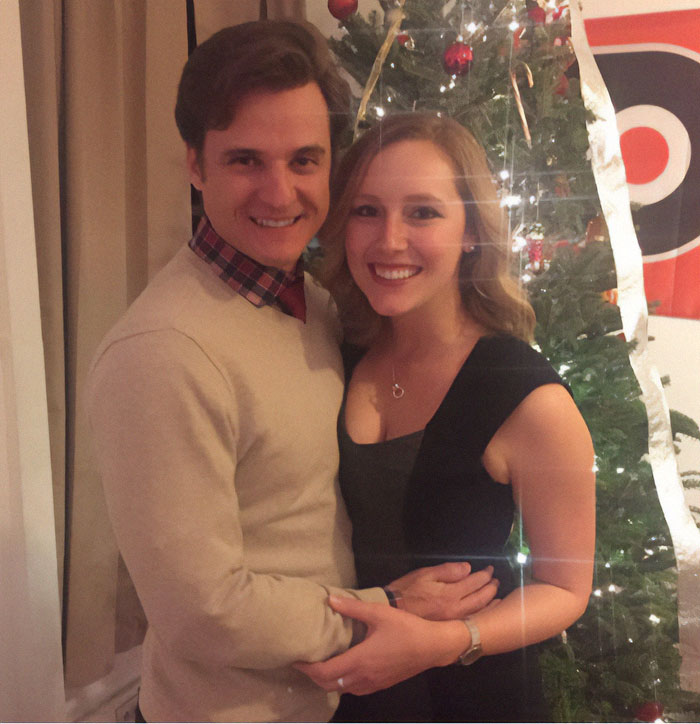 A couple smiling in front of a decorated Christmas tree, holding each other closely. A couple smiling in front of a decorated Christmas tree, holding each other closely.