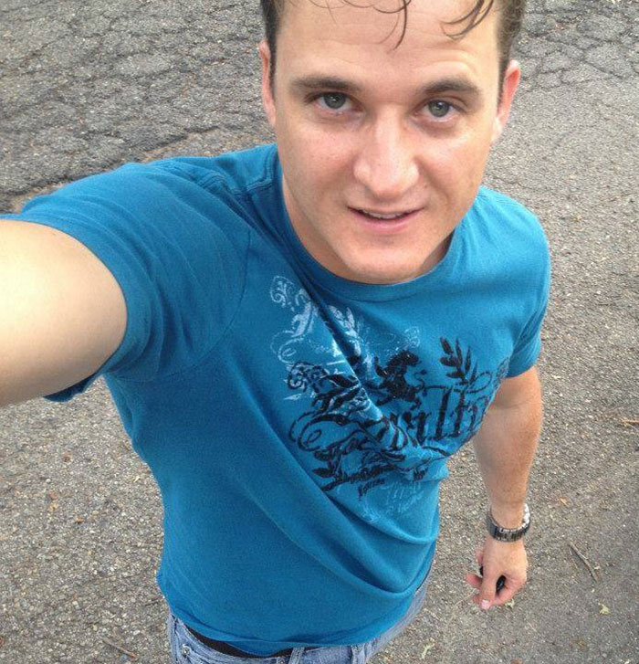 Man in a blue graphic tee taking a selfie outdoors; related to alleged cliff incident involving doctor. Man in a blue graphic tee taking a selfie outdoors; related to alleged cliff incident involving doctor.