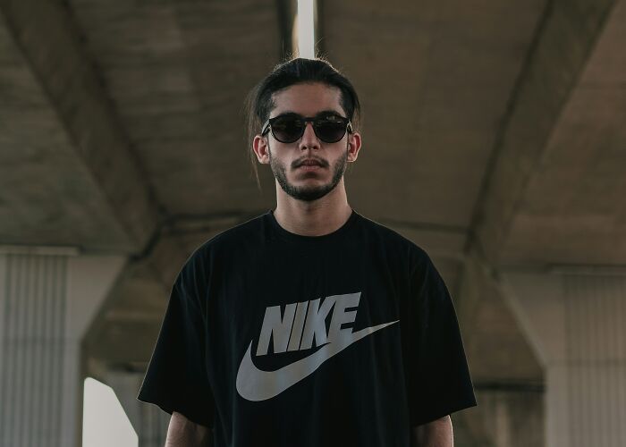 Young man wearing sunglasses and a black Nike shirt standing under a concrete structure with serious expression, depicting church quitting feelings.
