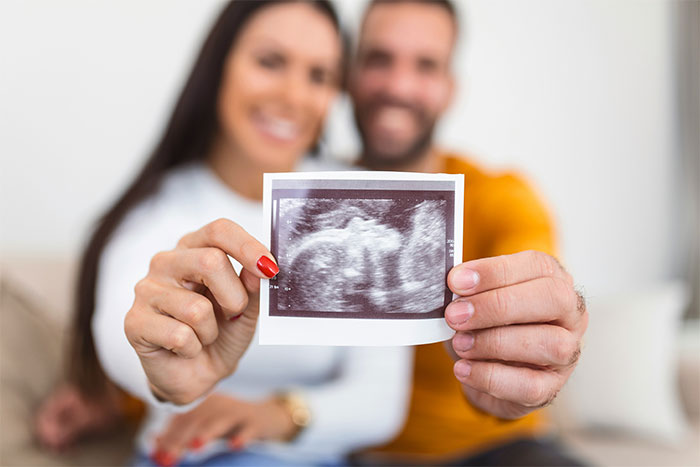Couple smiling and holding an ultrasound photo, representing their pregnancy announcement.