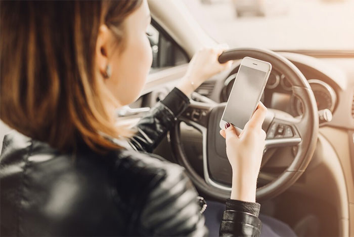 Woman driving a car, checking her smartphone for messages about partner's cheating, wearing a leather jacket.