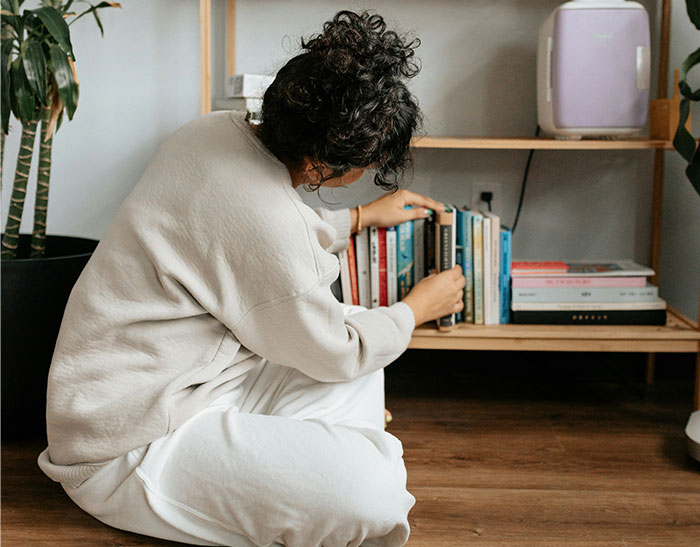 Person in a cozy setting looking at books on a shelf, reflecting on exposing a cheating partner.