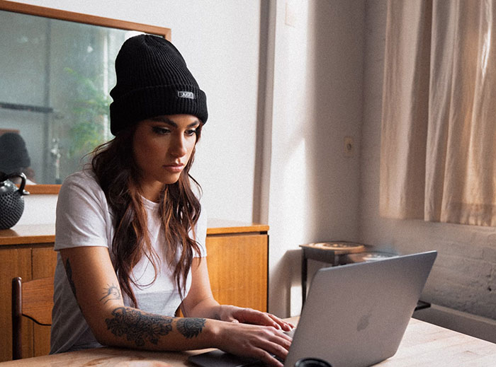 Woman in beanie using laptop, possibly discovering cheating partner online.