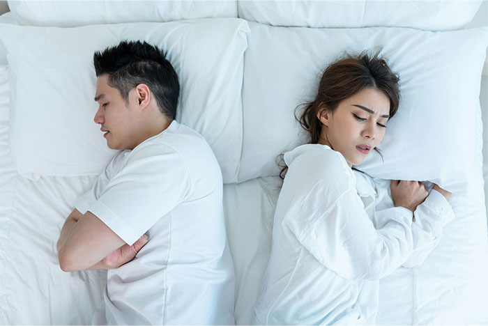 Couple lying back-to-back in bed, showing tension related to exposing a cheating partner.