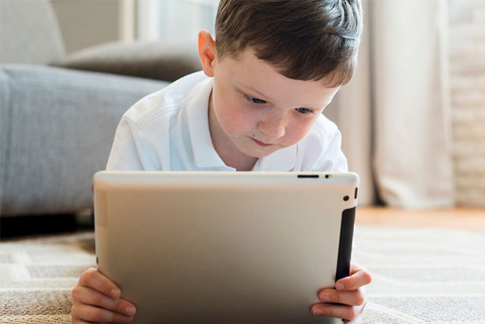 Child lying on floor using a tablet, focused and engaged.