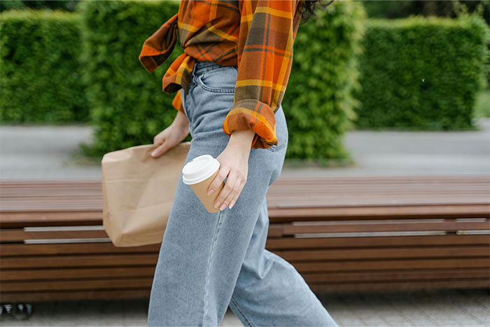 Person walking with a coffee cup and paper bag, wearing casual fall clothes, highlighting the theme of revealing a cheating partner.