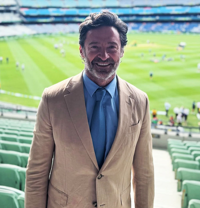 Hugh Jackman smiling at a stadium wearing a tan suit and blue shirt and tie as fans urge him to stay away from Ryan Reynolds and Blake Lively Hugh Jackman smiling at a stadium wearing a tan suit and blue shirt and tie as fans urge him to stay away from Ryan Reynolds and Blake Lively