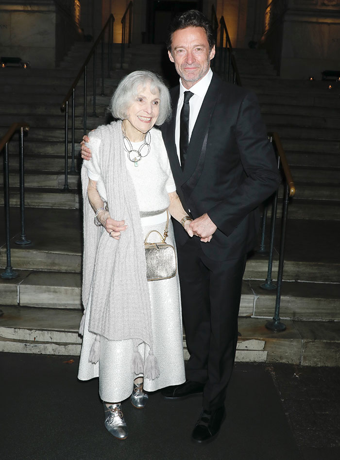 Hugh Jackman in formal attire, with an elderly woman, standing on steps at an event.