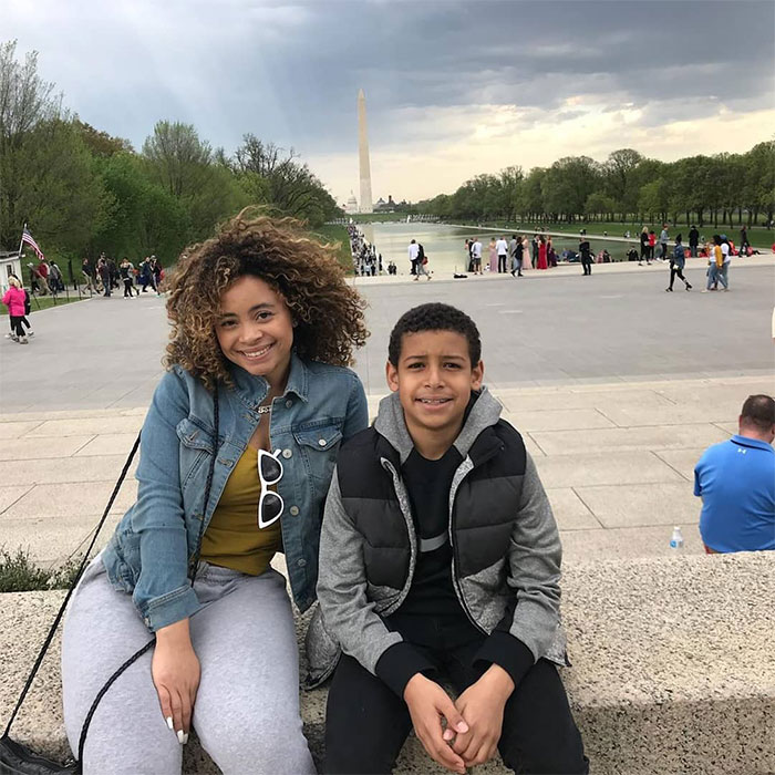 Ice Spice and her brother smiling by reflecting pool, with Washington Monument in view.
