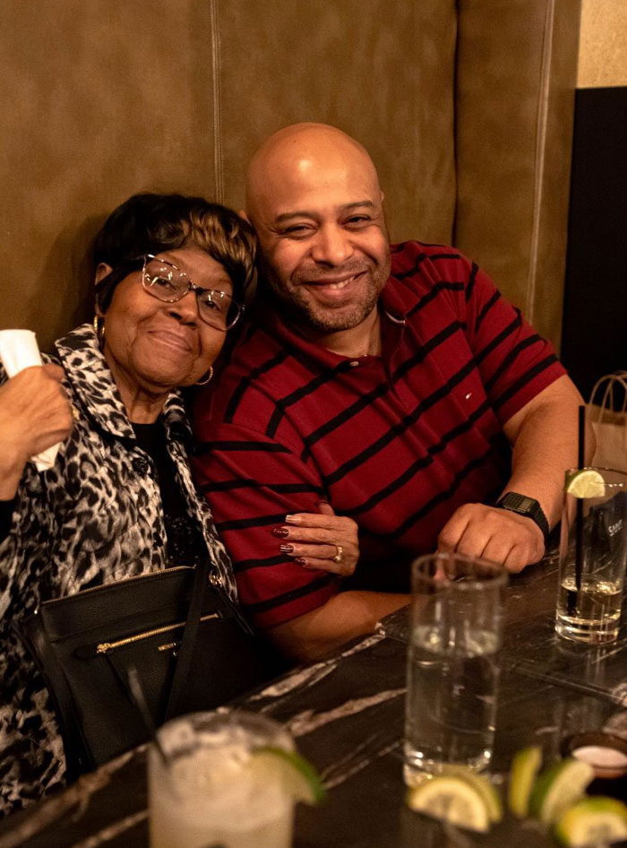 A happy duo at a restaurant table, capturing the essence of Ice Spice parents' warmth and joy, with drinks and lime wedges.