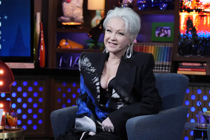 Cyndi Lauper in a studio setting, wearing a black and blue patterned outfit with striking earrings.