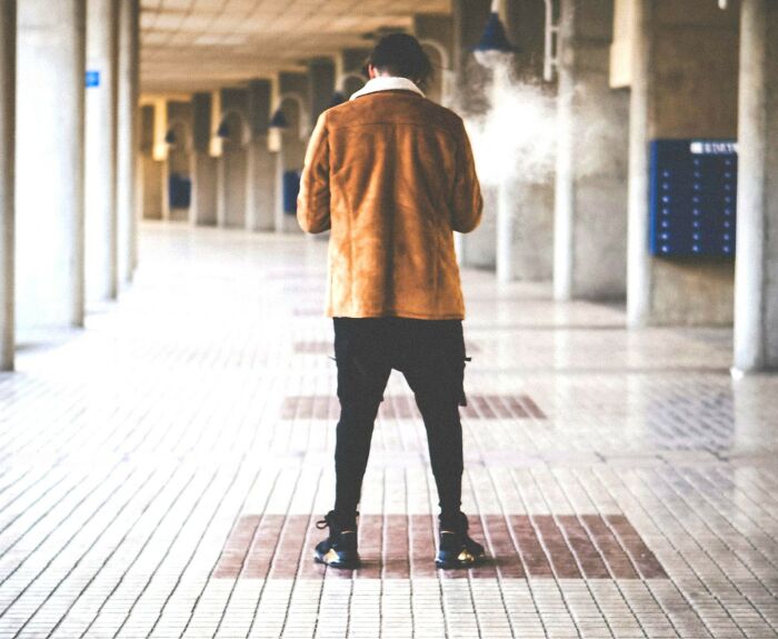 Person standing in a corridor wearing a brown jacket, surrounded by scattered dust. Disgusting scene witnessed.