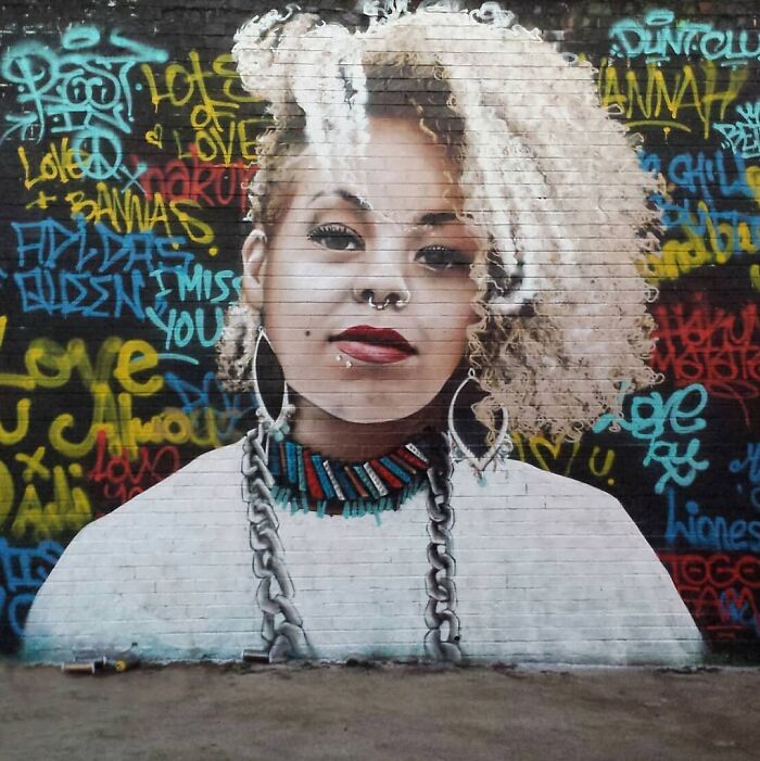 Mural of a woman with curly hair and bold jewelry on a vibrant graffiti-covered wall in Glasgow.