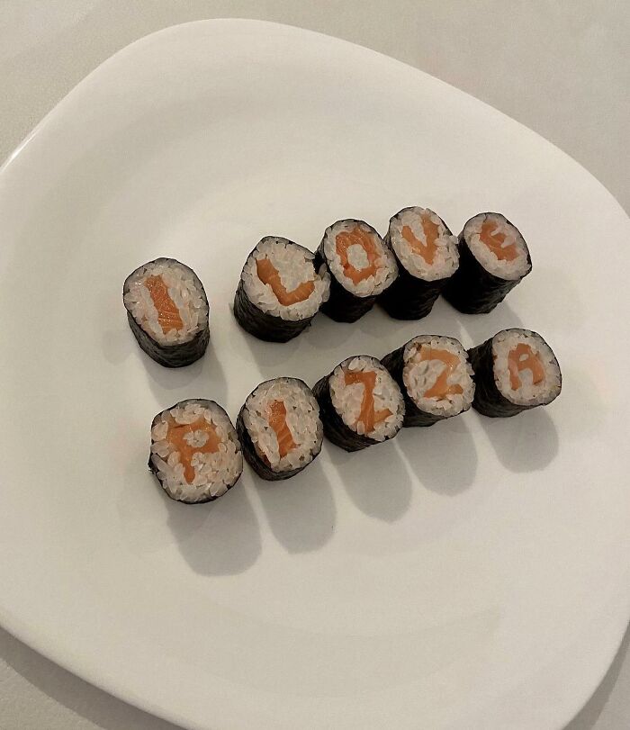 Sushi rolls spell "I love pizza" on a white plate, showcasing a unique artistic transformation.