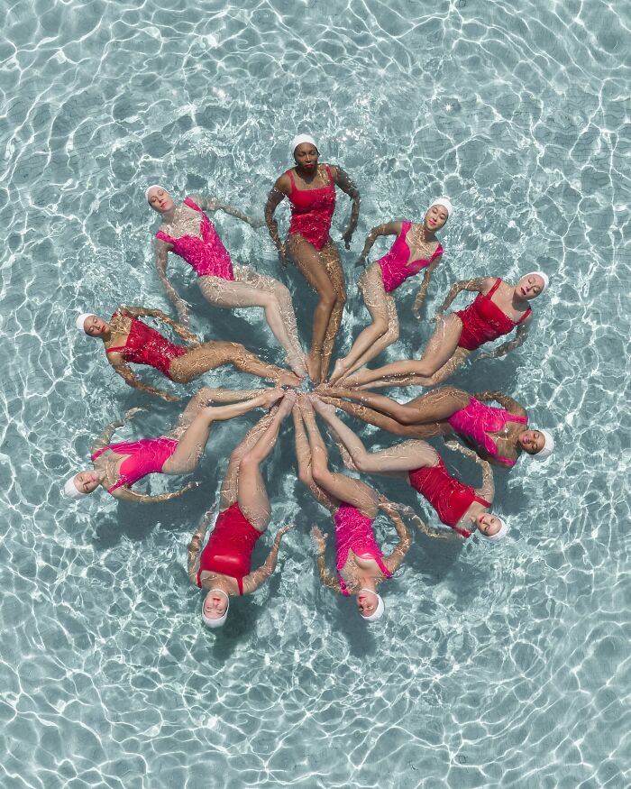 Aerial view of synchronized swimmers in pink suits forming a star pattern in a pool, showcasing conceptual photography.