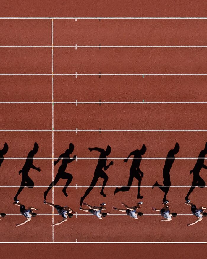 Aerial view of runners on a track casting long shadows, showcasing conceptual photography by Brad Walls.