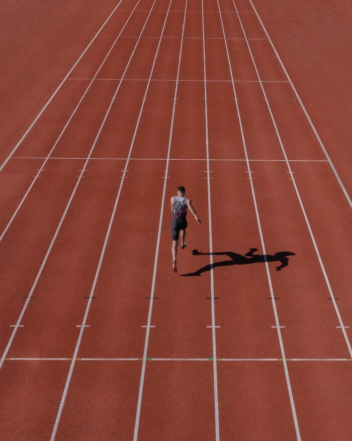 Aerial view of a runner on a track, casting a shadow, showcasing conceptual photography techniques.