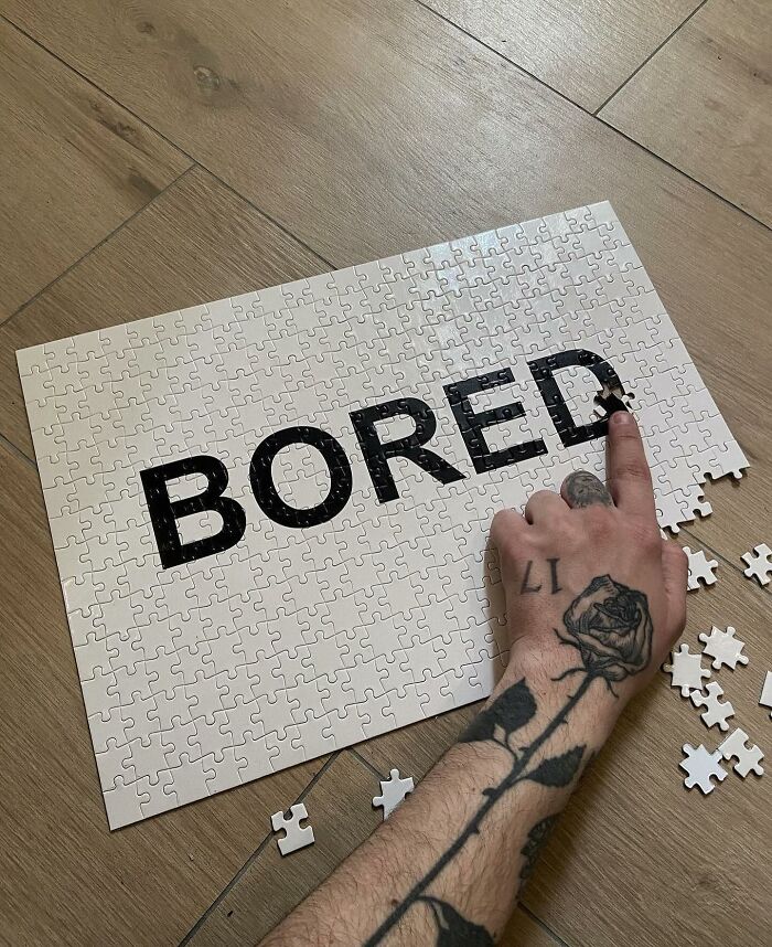 Puzzle artwork spelling "BORED," featuring a rose tattooed hand assembling the pieces on a wooden floor.