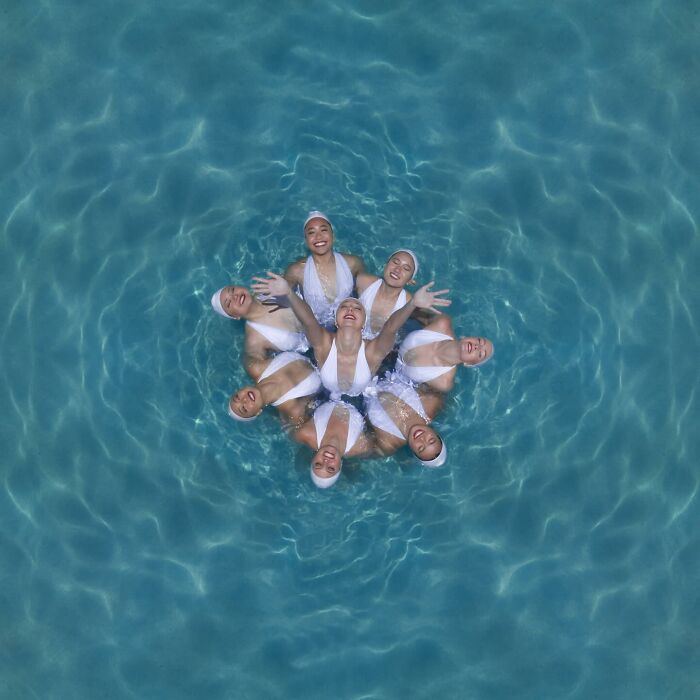Aerial conceptual photography of synchronized swimmers forming a star pattern in a pool.