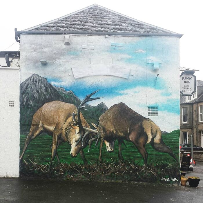 Mural in Glasgow of two stags fighting, set against a mountain backdrop on a building wall.
