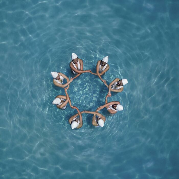 Aerial view of synchronized swimmers forming a circle in a pool, showcasing conceptual photography by Brad Walls.