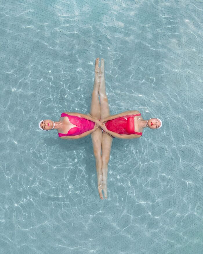 Aerial conceptual photography of two female swimmers in pink swimsuits forming geometric shape in a pool.