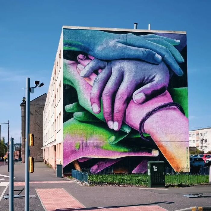 Colorful mural of intertwined hands on a building wall in Glasgow.